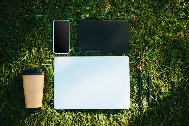 istock elevated view of digital devices and disposable coffee cup on green grass in park 1056670018