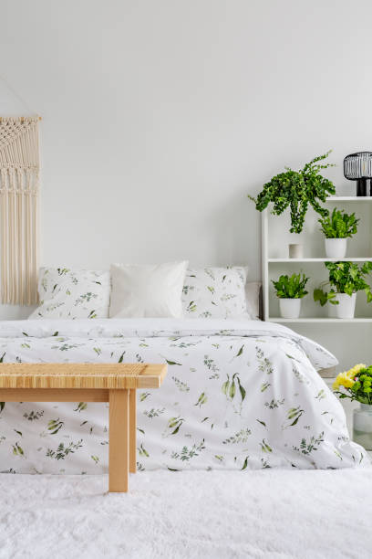 istock White bedroom interior with fresh plants on rack, floral sheets on double bed, carpet on the floor and empty place for your poster on the wall 1056672790