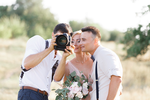 wedding photographer takes pictures of bride and groom in nature. photographer shows just taken photos to wedding couple