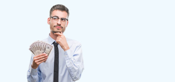 istock Young hipster business man holding dollars serious face thinking about question, very confused idea 1056680234