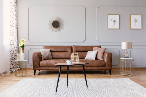 istock Wooden table on carpet in front of leather sofa in grey flat interior with posters and mirror. Real photo 1056681276