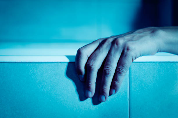 closeup of the hand of a young caucasian man on the side of a bathtub, in a creepy atmosphere