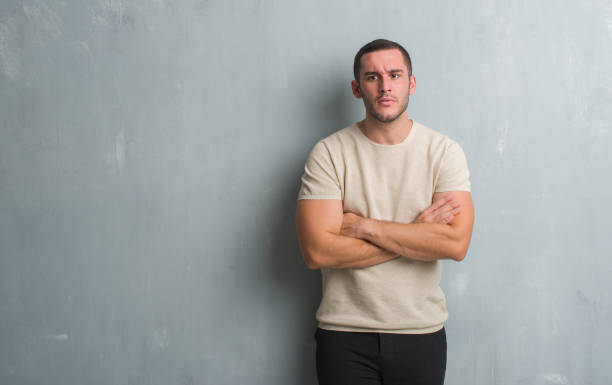 istock Young caucasian man over grey grunge wall skeptic and nervous, disapproving expression on face with crossed arms. Negative person. 1056688116