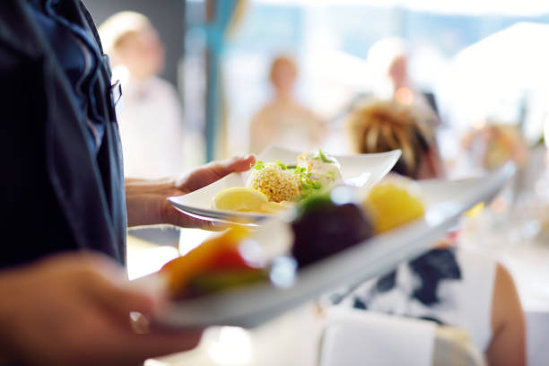Two unrecognisable waiters are coming out of a hotel kitchen while holding two dishes each, ready to serve to guests.