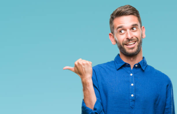 istock Young handsome man over isolated background smiling with happy face looking and pointing to the side with thumb up. 1056716200