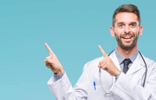 istock Young handsome doctor man over isolated background smiling and looking at the camera pointing with two hands and fingers to the side. 1056716312