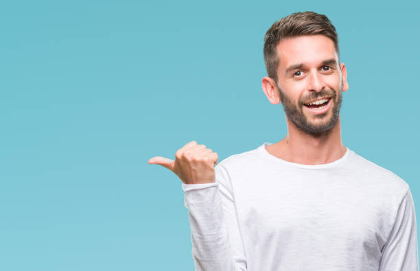 istock Young handsome man over isolated background smiling with happy face looking and pointing to the side with thumb up. 1056716366