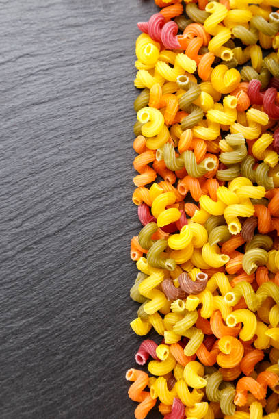 istock multicolored spiral pasta scattered on a black slate background. 1056735780