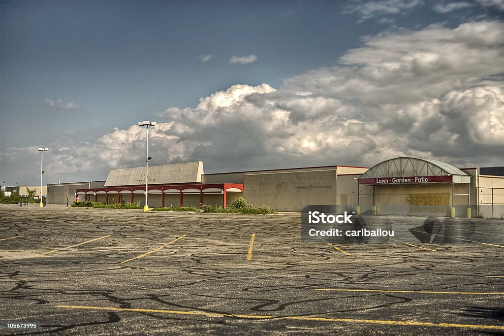 Vacant commercial store parking lot An empty, vacant commercial store with overgrown weeds and empty parking lot in the foreground. Abandoned Stock Photo