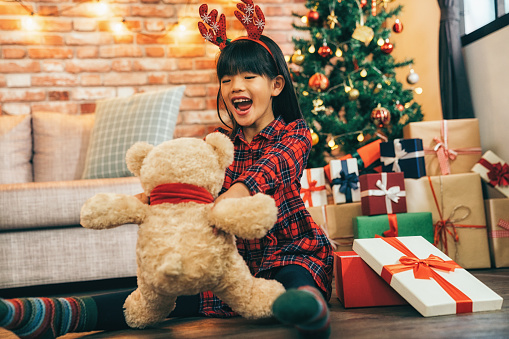 cute child holding teddy bear being joyful fresh and cheerful. attractive girl childhood at home celebrates Christmas. many gifts around the tree in the sweet living room.