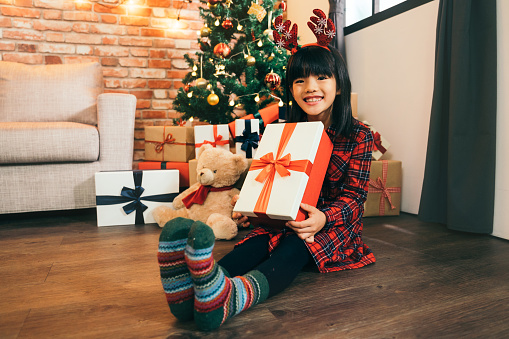 lovely daughter with colorful green socks holding christmas present with red ribbon. Happy little smiling girl with Christmas gift box. Happy Christmas - Kid with gift from santa.
