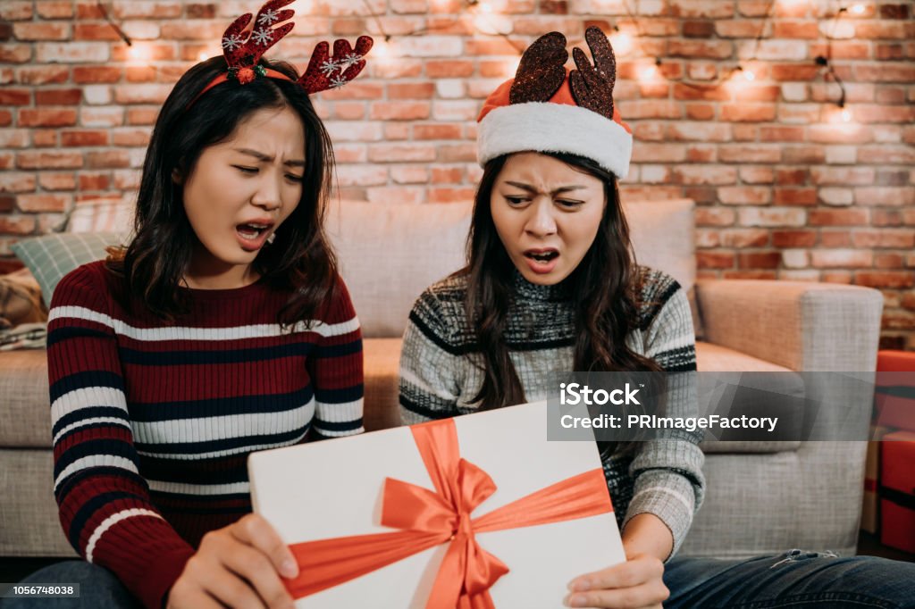 girls open gift box at home feeling displeased sisters received a terrible present from online shopping. young girls open gift box day at home feeling displeased. grumpy girls in santa hats buying clothes from christmas sale. Arrival Stock Photo