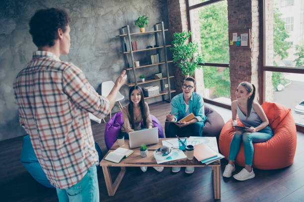 quatro adoráveis inteligentes, espertos, inteligentes pessoas, amigos em jeans casual. meninas bonitas e bonito nerd pessoal, alto-falante de relatório, explicando os planos do projeto, crescimento do lucro do rendimento, reunião, reunindo - computer team young adult smart casual - fotografias e filmes do acervo