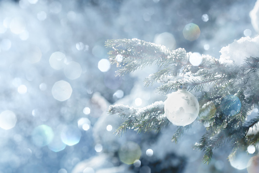 Winter scene with defocused lights and white Christmas bauble in sunlight