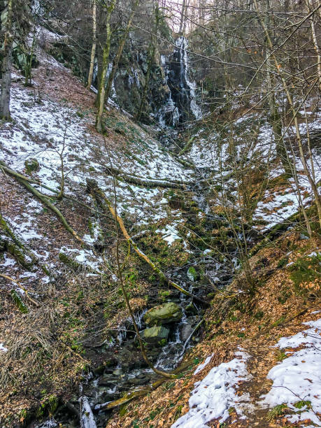 istock Frozen waterfall with icicles and a small stream with rocks in a forest landscape of Wasserfall Germany 1056766512