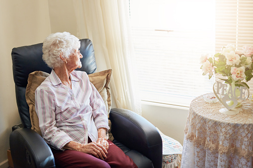 Shot of an elderly woman relaxing on a chair at home and looking thoughtfully out the window