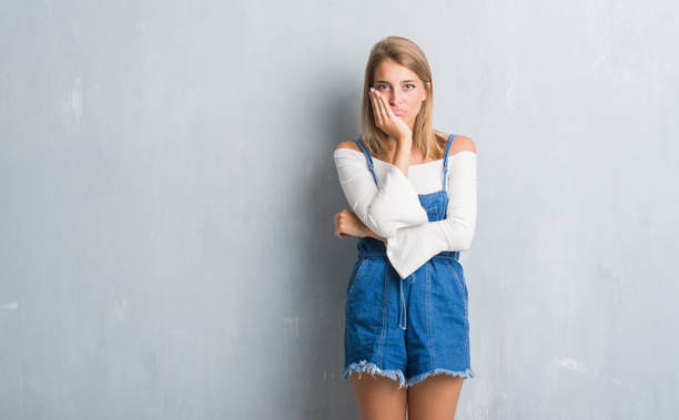 istock Beautiful young woman standing over grunge grey wall thinking looking tired and bored with depression problems with crossed arms. 1056777554