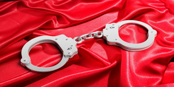 istock Metal handcuffs on red satin background, 3d illustration 1056779180