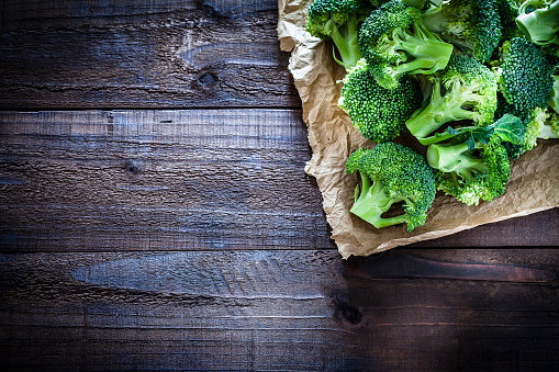 Fresh organic broccoli on crumpled brown paper arranged at the top-right corner of an old weathered wooden table. Useful copy space left for text and/or logo. Predominant colors are green and brown. Low key DSRL studio photo taken with Canon EOS 5D Mk II and Canon EF 100mm f/2.8L Macro IS USM.