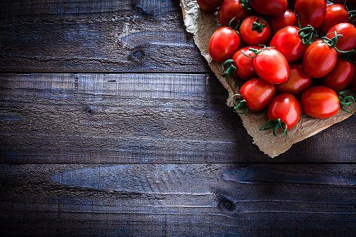 Fresh organic ripe tomatoes on crumpled brown paper arranged at the top-right corner of an old weathered wooden table. Useful copy space left for text and/or logo. Predominant colors are red and brown. Low key DSRL studio photo taken with Canon EOS 5D Mk II and Canon EF 100mm f/2.8L Macro IS USM.