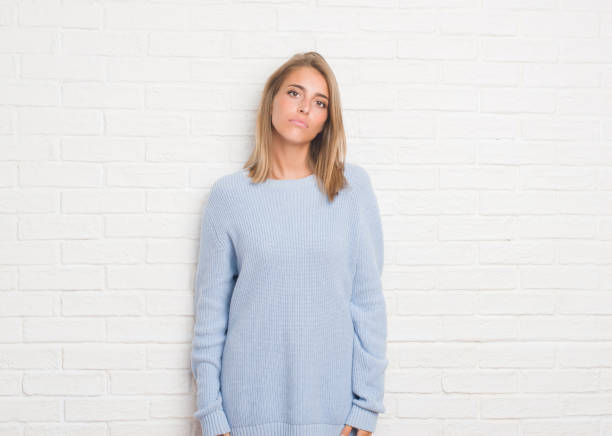 istock Beautiful young woman over white brick wall with serious expression on face. Simple and natural looking at the camera. 1056782868