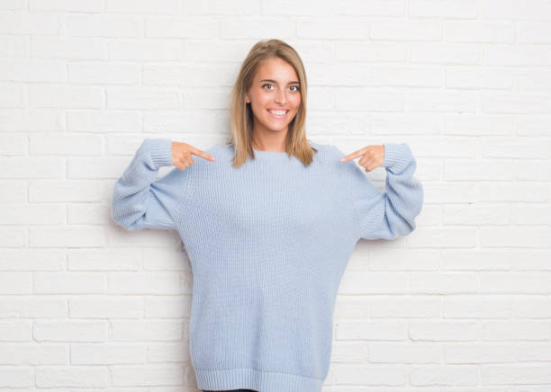 istock Beautiful young woman over white brick wall looking confident with smile on face, pointing oneself with fingers proud and happy. 1056782898