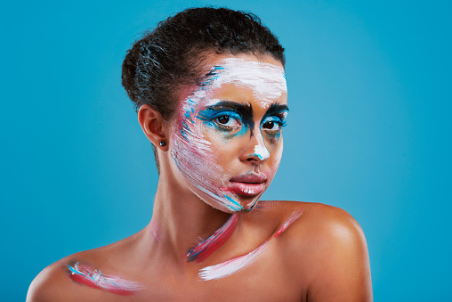 Studio portrait of a beautiful young woman covered in face paint posing against a blue background