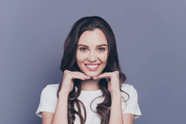 retrato do magnífico bom encantador adorável alegre encaracolados menina elegante casual camiseta branca, segurando o queixo nas mãos, isoladas sobre fundo cinzento - dental cosmetic - fotografias e filmes do acervo