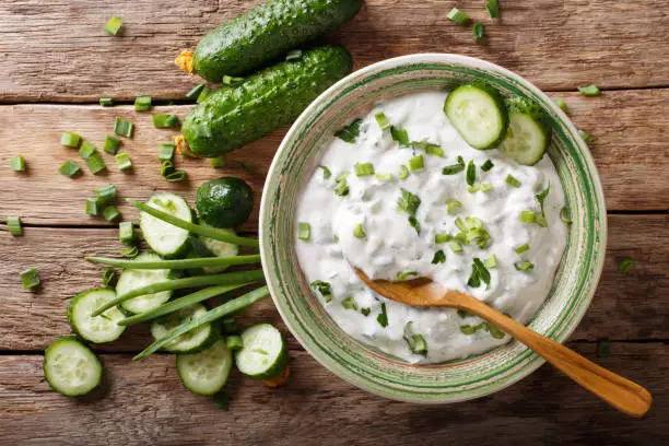 Indian spicy sauce raita with herbs and cucumber close-up in a bowl on the table. horizontal top view from above