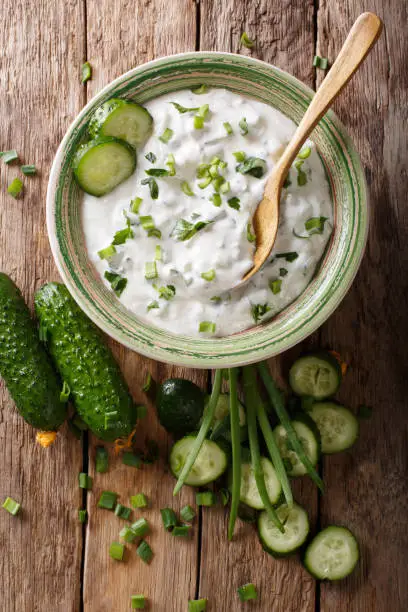 Indian spicy sauce raita with herbs and cucumber close-up in a bowl on the table. Vertical top view from above