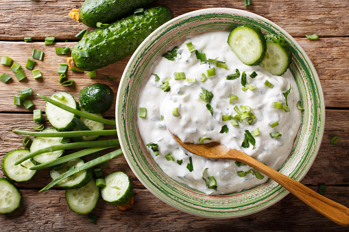 sauce of yogurt with herbs, spices and cucumber close-up in a bowl on the table. raita. horizontal top view from above