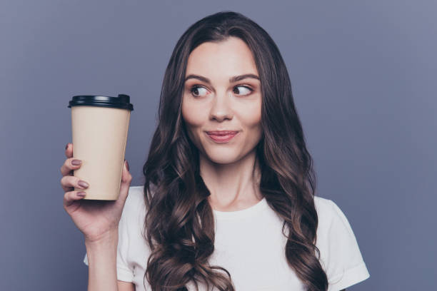 close-up portrait of attractive pretty lovely stylish nice cute cheerful curly-haired brunette girl in casual white t-shirt, holding, looking at paper-cup coffee, isolated on grey background - coffee take out food cup paper imagens e fotografias de stock