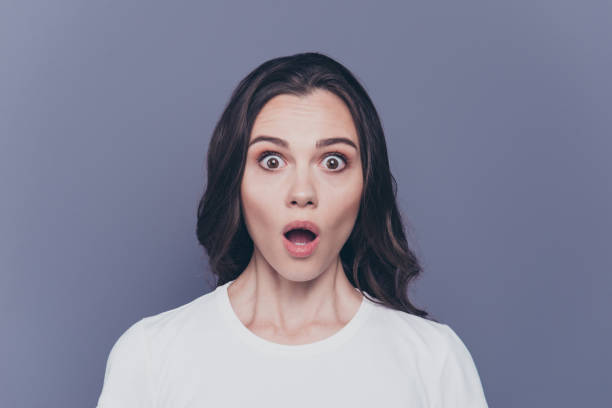 portrait de séduisante jolie charme élégant peur jeune fille aux cheveux bouclés brune en casual t-shirt blanc avec ses gros yeux et la bouche ouverte, isolé sur fond gris - bad habit fear emotional stress women photos et images de collection