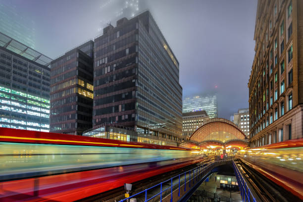 View to the Canary Wharf train station, London, United Kingdom View to the Canary Wharf train station with moving trains on a foggy winter evening, London, United Kingdom london docklands stock pictures, royalty-free photos & images