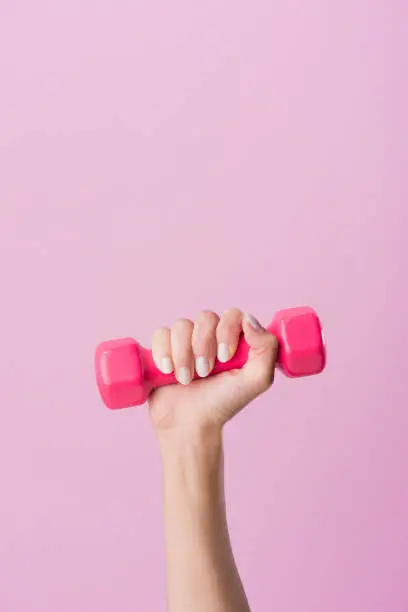 Photo of cropped shot of woman holding dumbbell isolated on pink