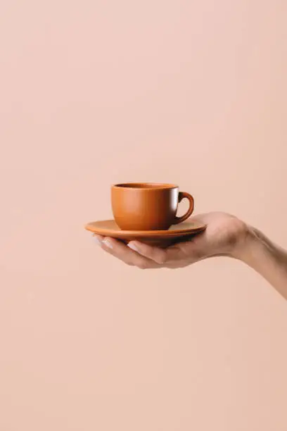 Photo of cropped shot of woman holding cup of coffee isolated on beige