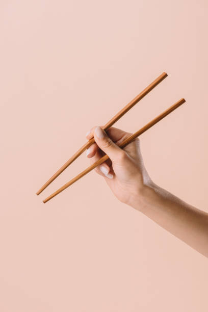 tiro cortado de mujer sosteniendo los palillos aislados en beige - chopsticks fotografías e imágenes de stock