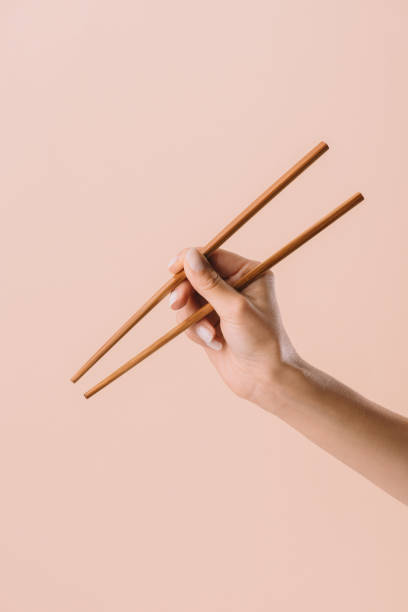 foto recortada de mulher segurando os pauzinhos isolados em bege - chopsticks human hand women isolated - fotografias e filmes do acervo