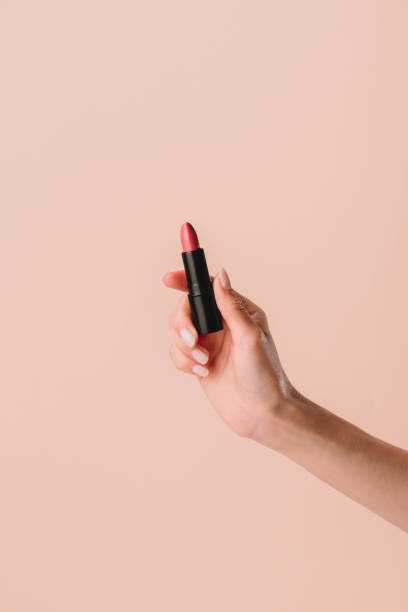 cropped shot of woman holding lipstick isolated on beige cropped shot of woman holding lipstick isolated on beige lipstick stock pictures, royalty-free photos & images