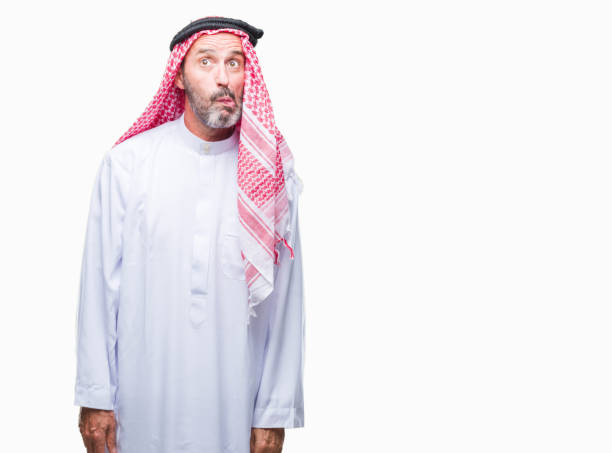 istock Senior arab man wearing keffiyeh over isolated background making fish face with lips, crazy and comical gesture. Funny expression. 1056797924