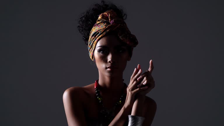 black ethnicity : Beautiful Sexy Black Woman,Young beautiful fashion model with traditional african style with scarf, earrings and makeup on dark background.Side view portrait of dark skinned model on a black backstage. Light and shadow portrait of a woman in side view.