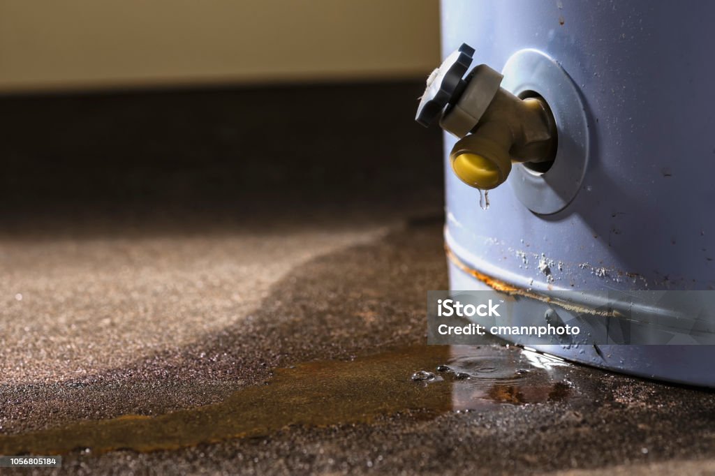 A leaking faucet on a domestic water heater Water leaking from the plastic faucet on a residential electric water heater sitting on a concrete floor. Boiler Stock Photo