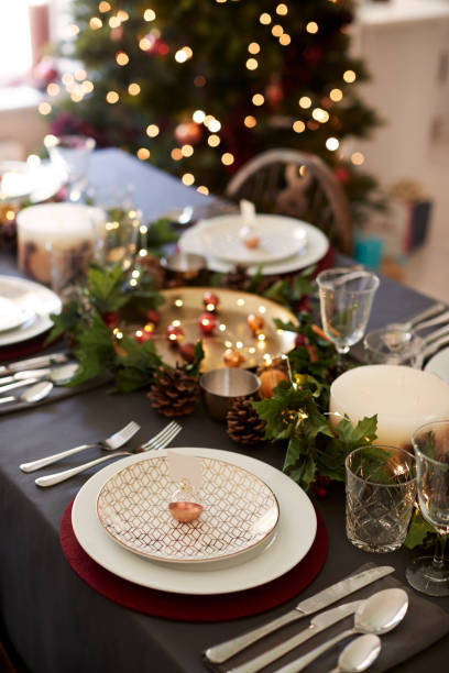 istock Christmas table setting with bauble name card holder arranged on a plate and green and red table decorations, Christmas tree in the background, elevated view 1056806310