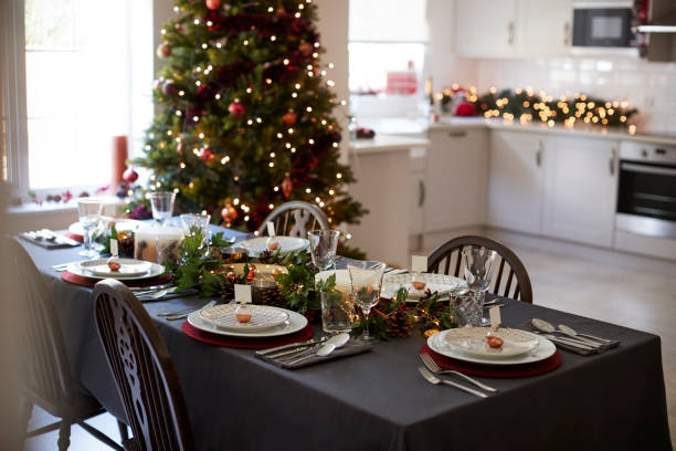 istock Christmas table setting with bauble name card holders arranged on plates and green and red decorations with Christmas tree and kitchen in the background 1056806366