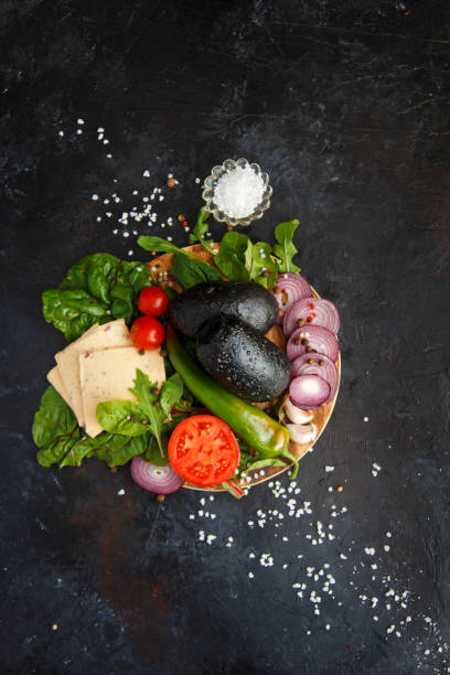 Ingredients for Veggie Hamburger or Salad Cheese Fresh Greens, Arugula, Chard, Pepper, Chili, Tomatoes, Cherry, Cucumber, Onion, Fresh Bread on a dark background