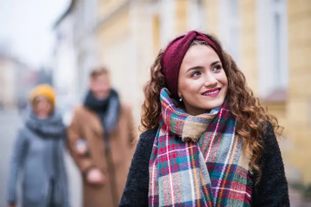 A portrait of teenage girl with headband and scarf standing on the street in winter. Christmas shopping concept.