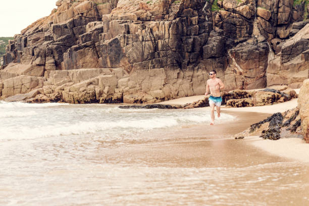 istock Man running along the shoreline of Pedn Vounder Beach, Cornwall on a June day. 1056830256