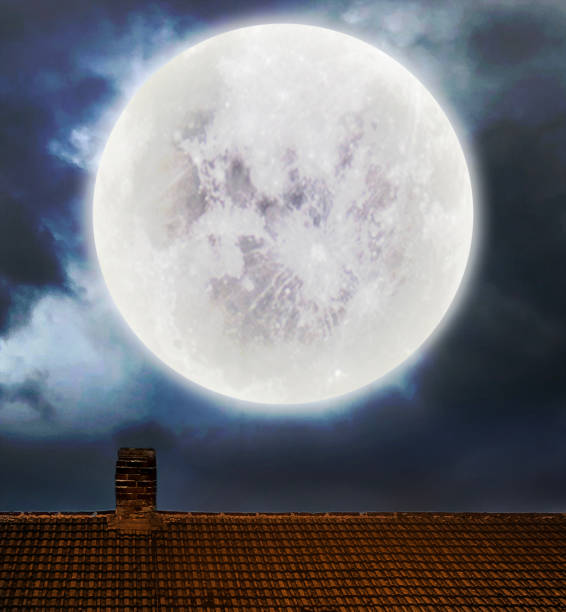 Halloween illustration with bluish tones, a crow calling at the top of the roof across the full moon on a hazy sky.