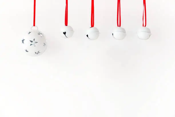 White Christmas jingle bells with red ribbon hanging in front of white background.