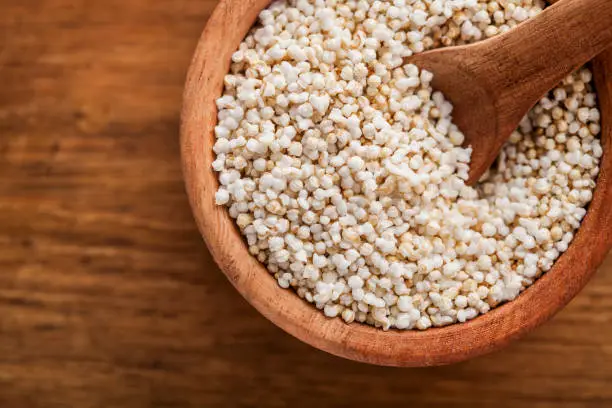 close up of popped or puffed amaranth in a wooden bowl and wooden background, with wooden spoon